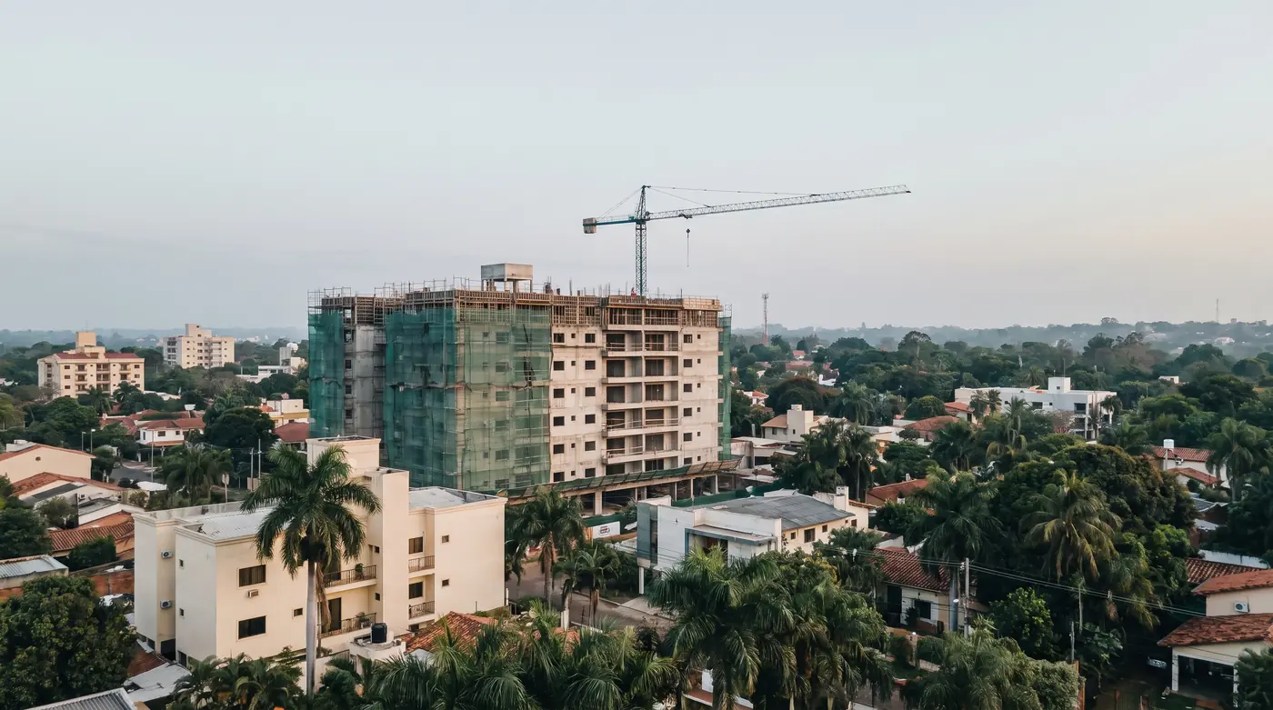 Residential building under construction with a tower crane in Asuncion, surrounded by low houses and palm trees